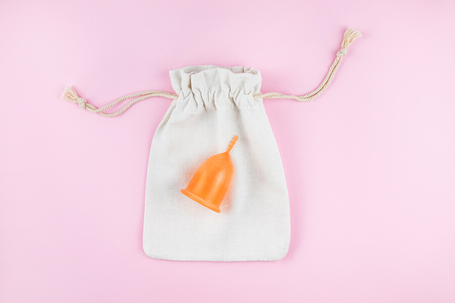 an orange menstrual cup sat on top of a cotton storage bag