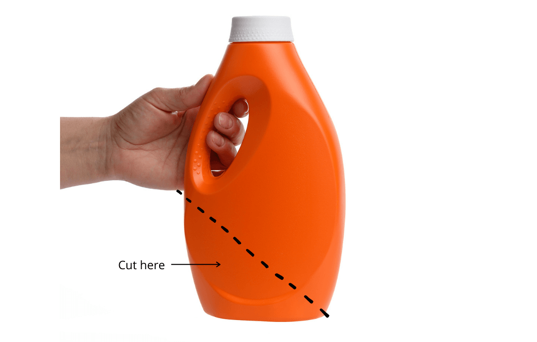 An orange plastic bottle being held in the air by a hand, with a dotted line that shows where to cut the bottle in order to create a scoop 