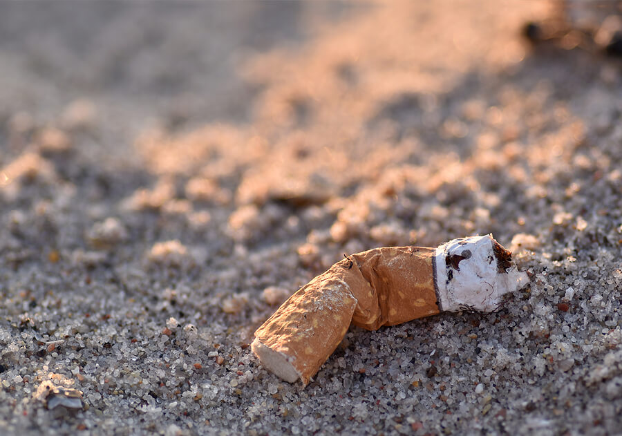 A weathered cigarette butt sat on a sandy beach as litter