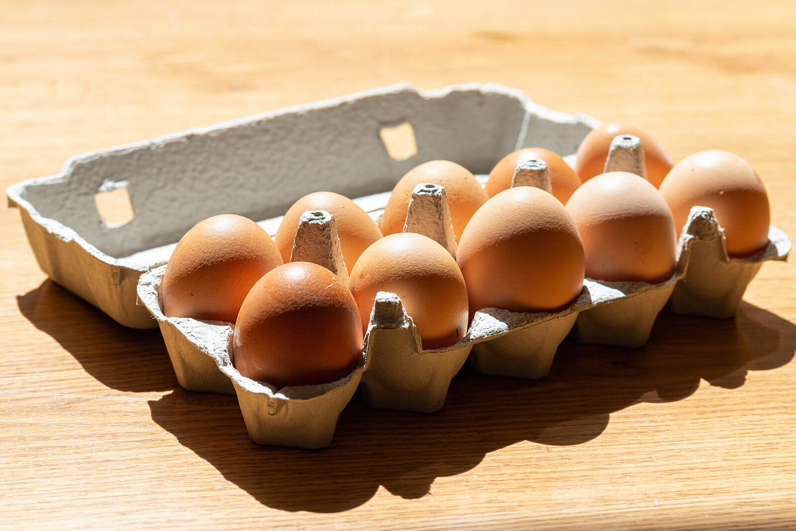 An egg carton containing 10 fresh chicken eggs, placed on a light-coloured table