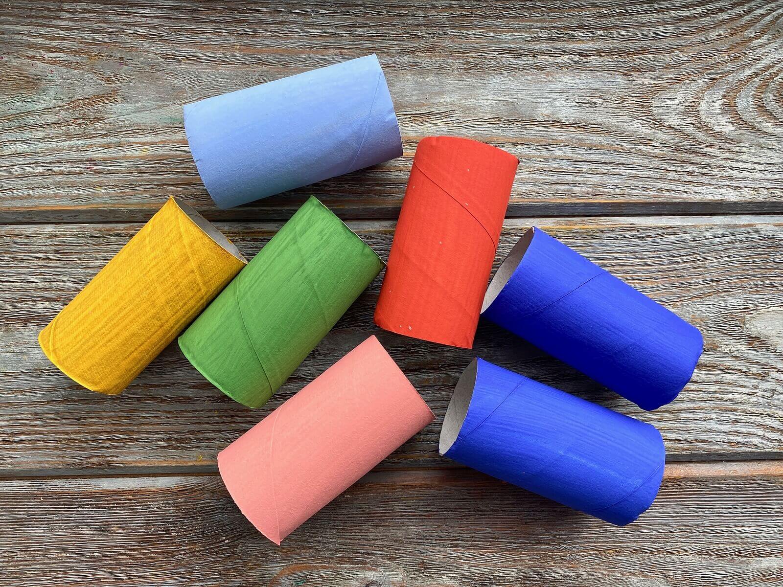Toilet roll tubes painted in various block colours, presented on a wooden table.