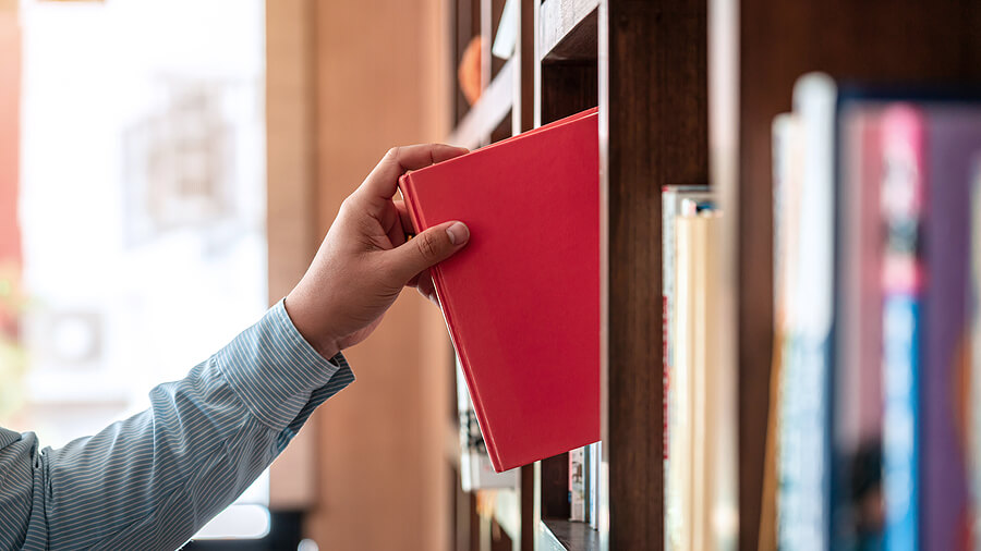 Close up of asian man checking interesting book from bookcase to searching a book and taking off book from the bookshelf in library while reading a book to relaxation from work hard