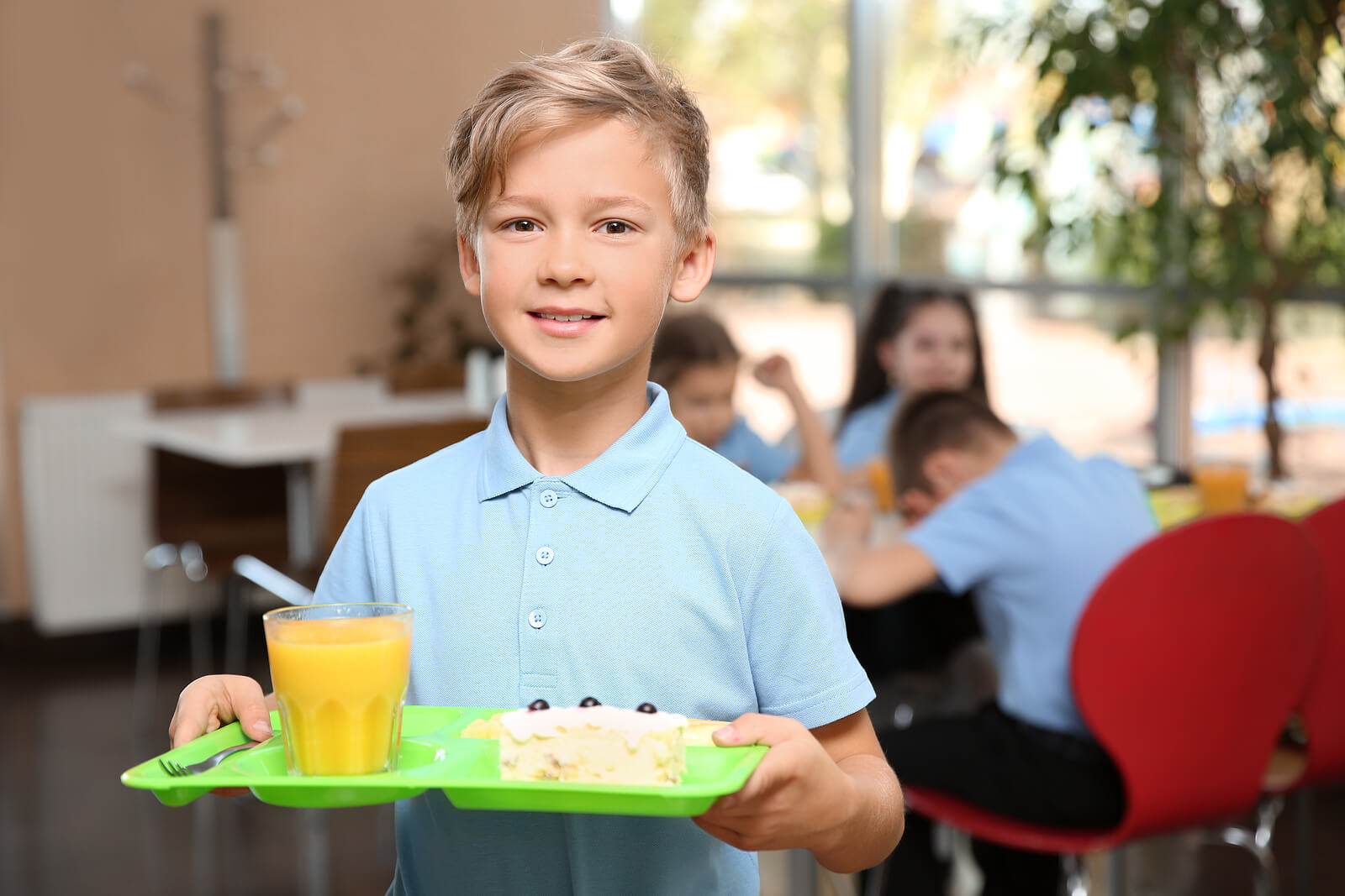 A schoolboy holding a lunch tray that has cake and orange juice on it.