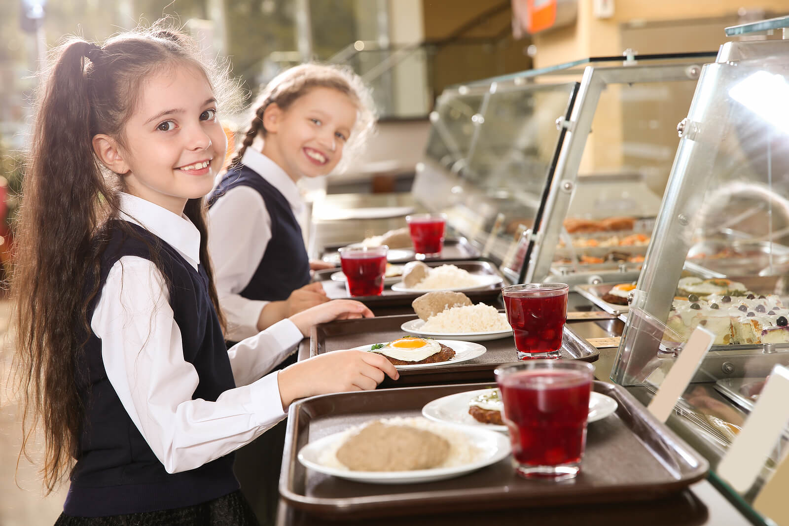 Two schoolgirls collecting their lunch on trays in the school canteen.