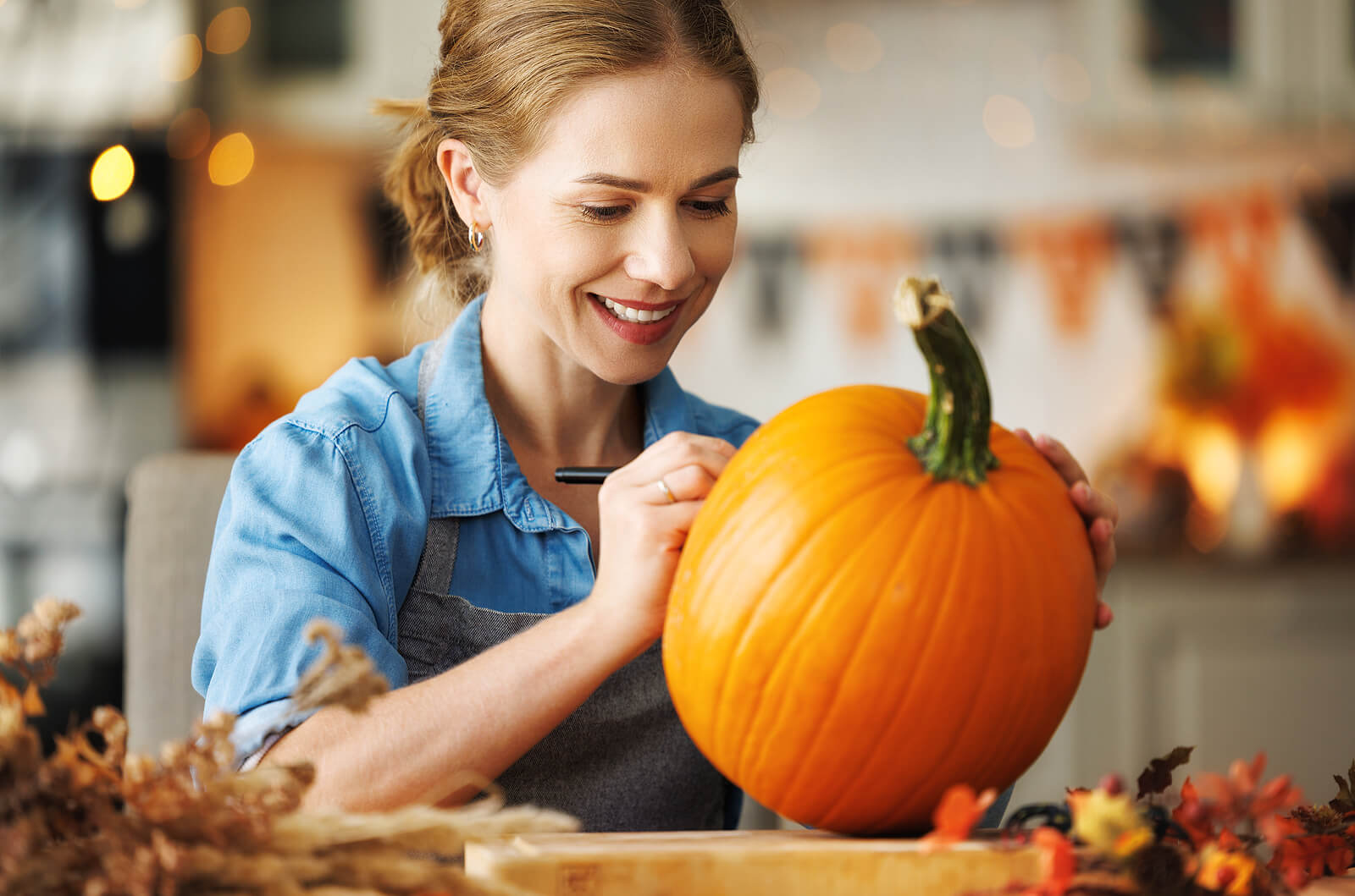 A woman painting a pumpkin while wearing an apron.