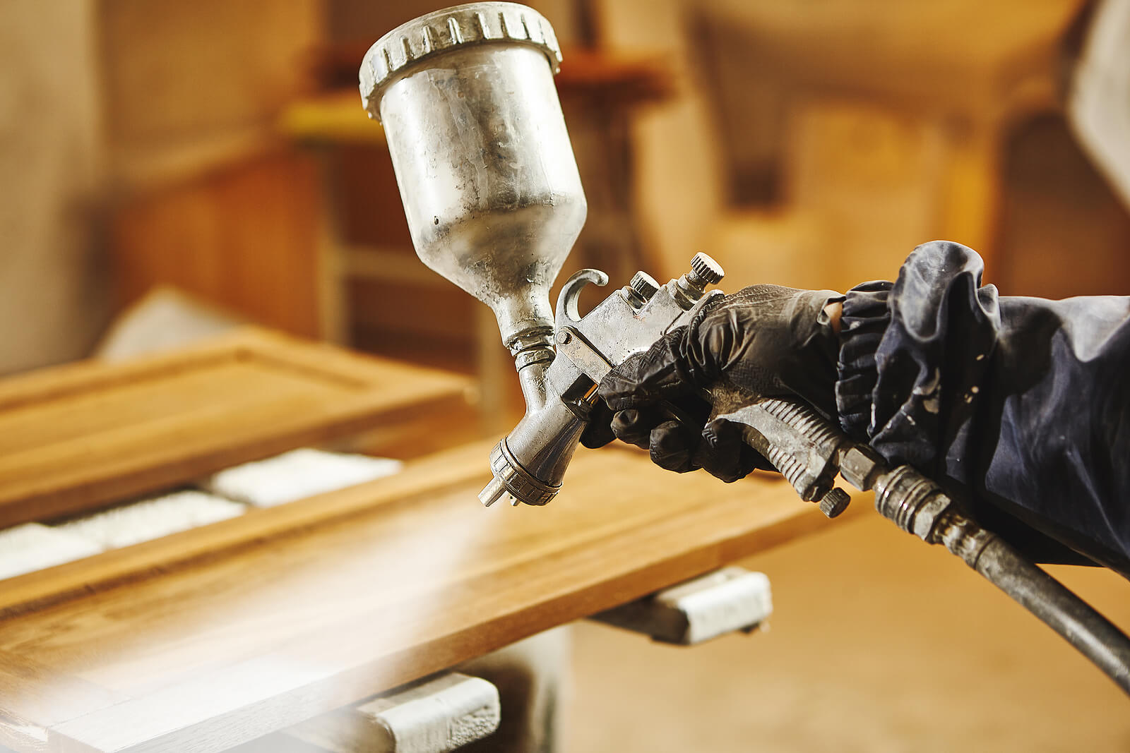 Varnish being applied to a kitchen cabinet door with a spray gun.