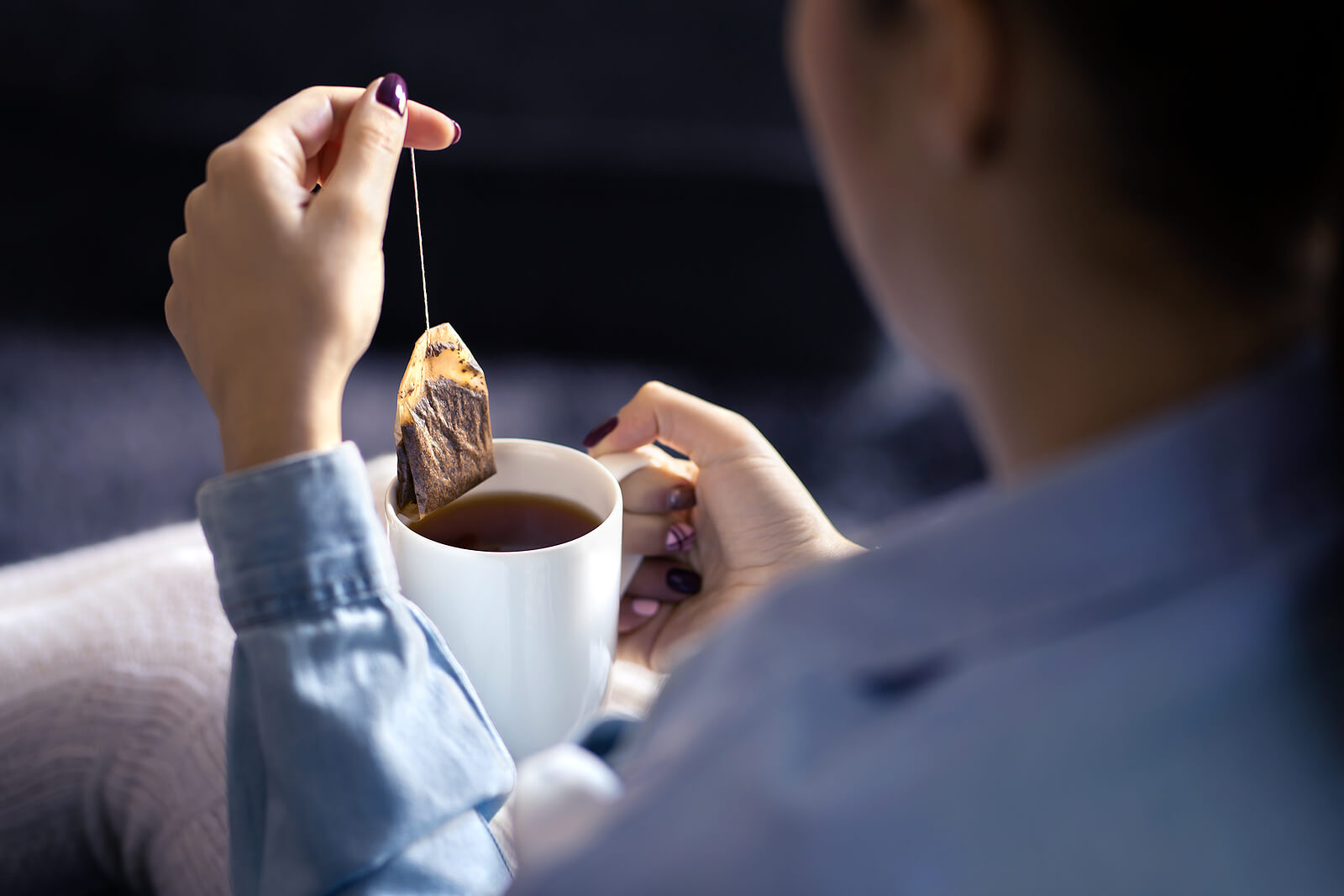 A woman pulling a teabag out of a cup