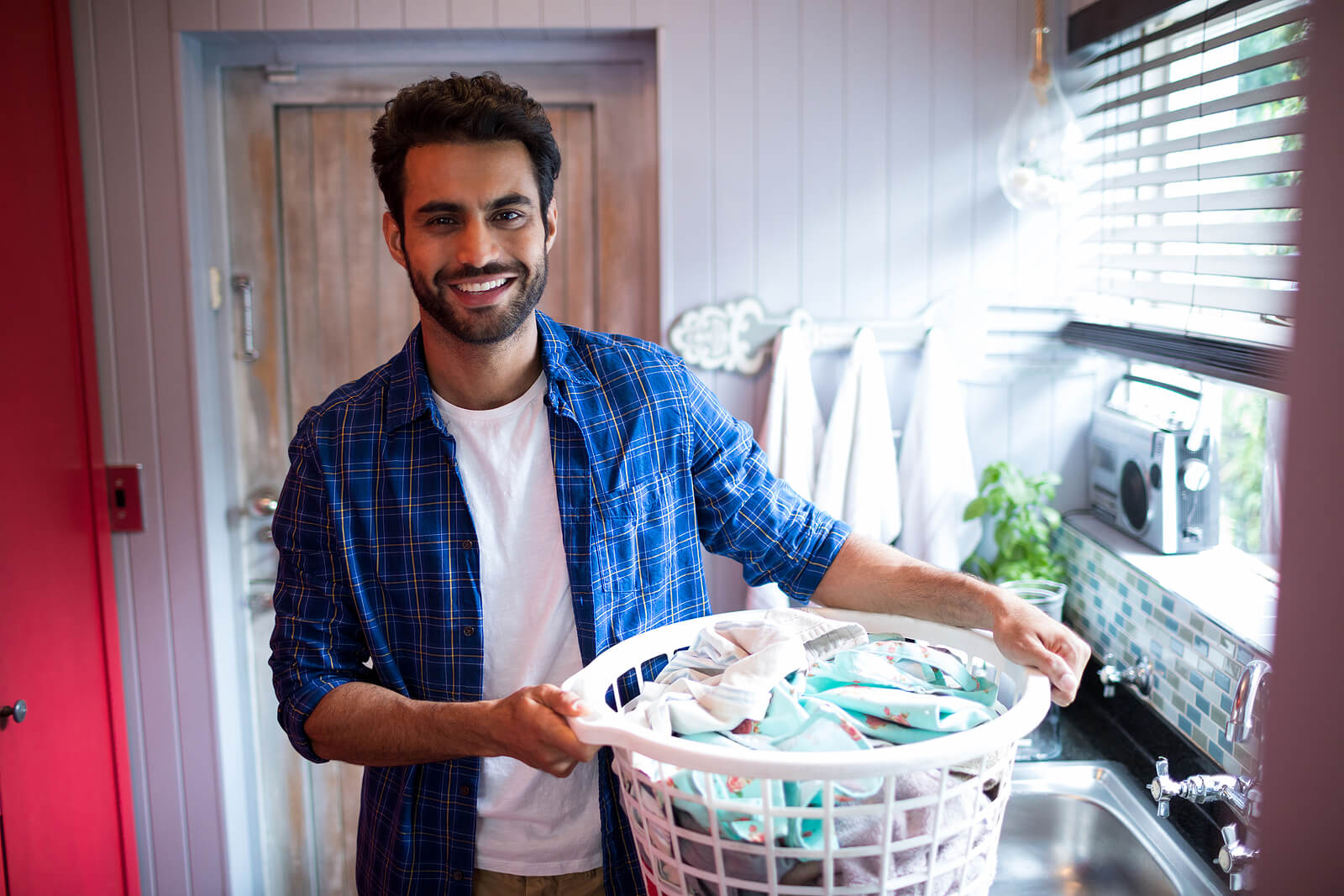 A happy man holding a laundry basket next to a window.