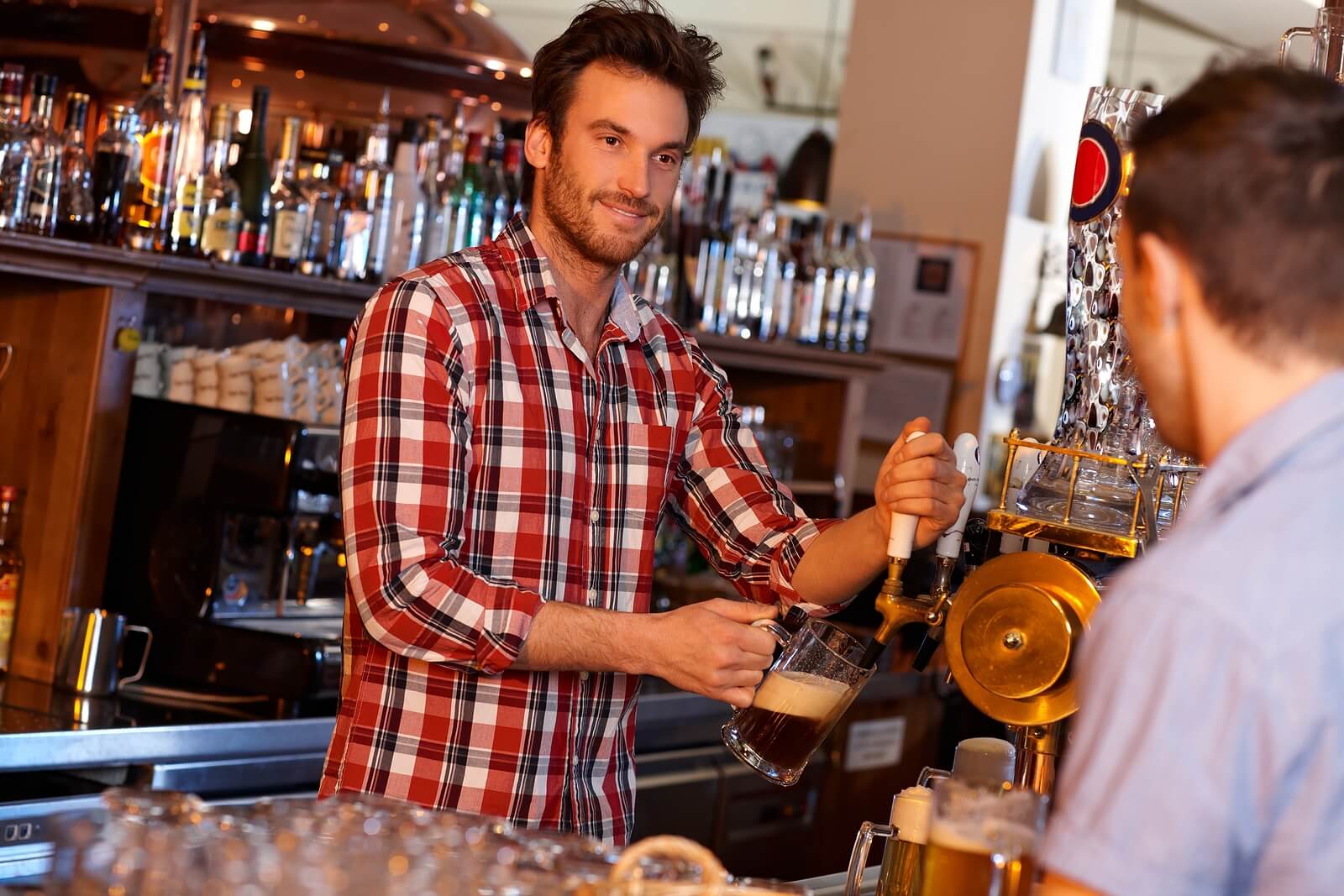 A bartender pouring a pint behind the bar while smiling at the customer.