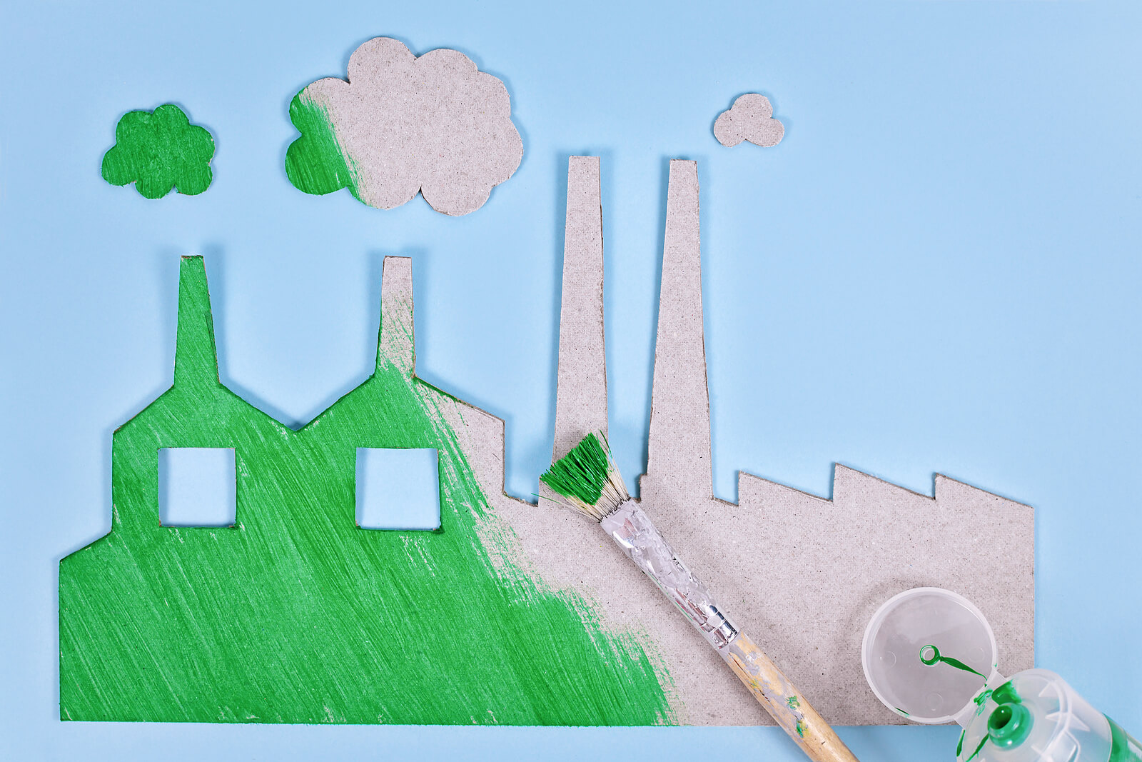 A factory made of cardboard being painted green to represent the concept of greenwashing.