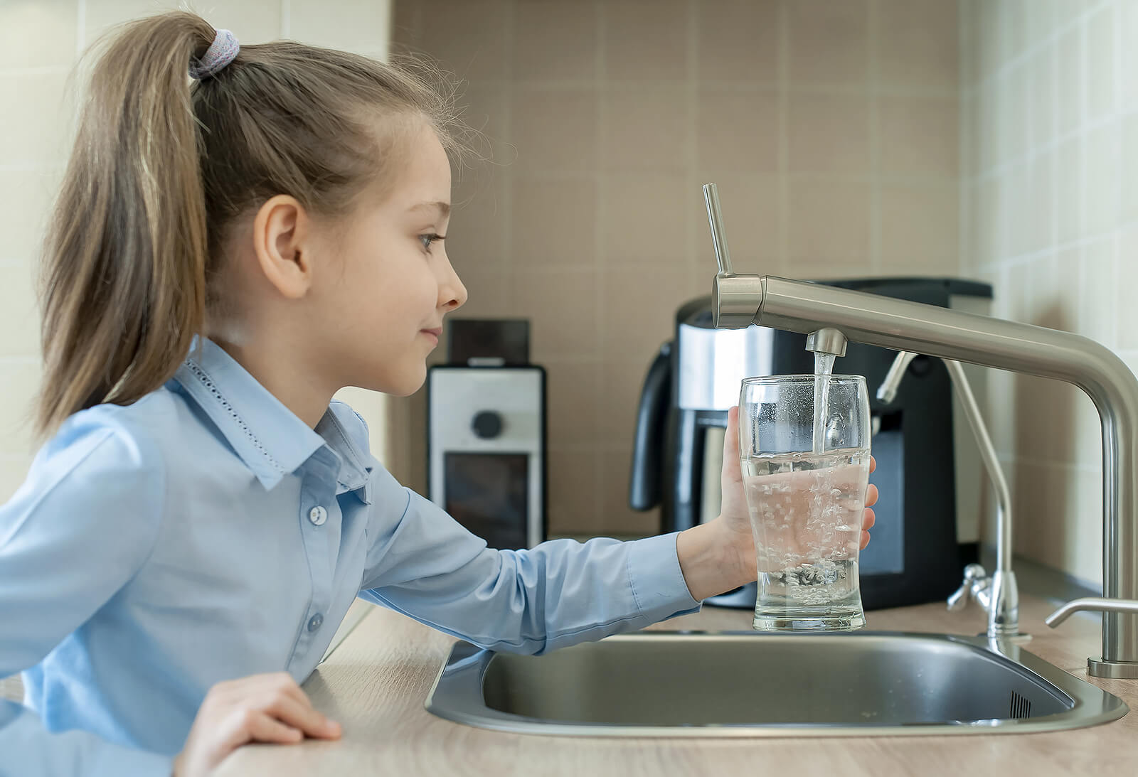 A girl in a school uniform running a tap to fill a glass with water.